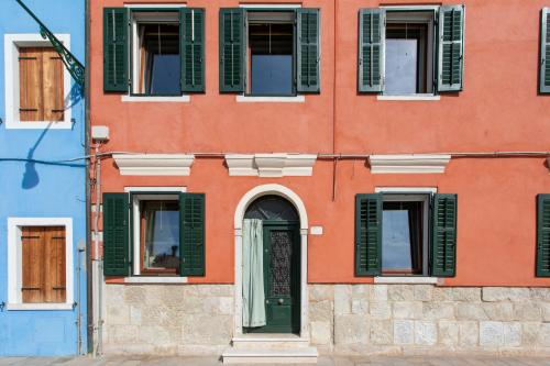 an orange building with green shuttered windows at Wondrous Palazzetto 1619 in Magical Burano Island in Burano