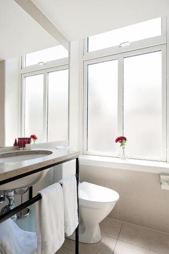 a bathroom with a toilet and a sink and two windows at Elite Stadshotellet Växjö in Växjö