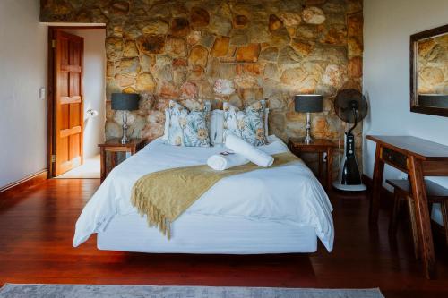 a bedroom with a bed and a stone wall at Blue Crane Farm Lodge in Botrivier