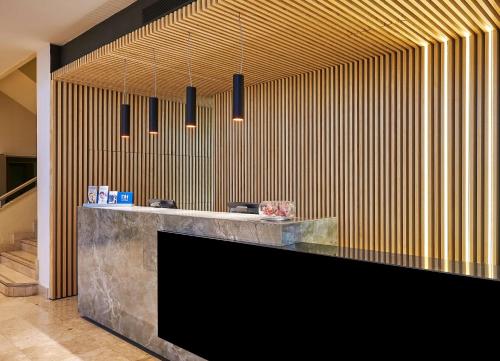 a lobby with a black counter and wooden wall at NH Luz Huelva in Huelva