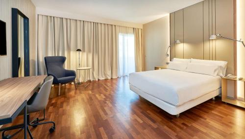 a hotel room with a white bed and a desk at NH Luz Huelva in Huelva