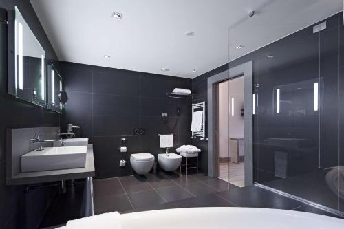 Baño negro con 2 aseos y lavamanos en NH Parma, en Parma