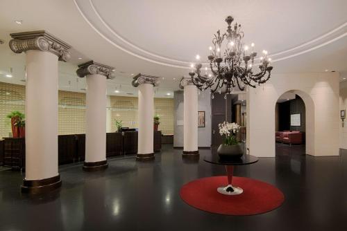 un gran vestíbulo con una lámpara de araña y una alfombra roja en NH Siena en Siena