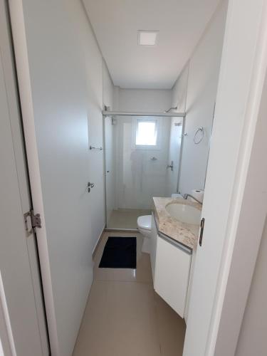 a white bathroom with a toilet and a sink at Lindo apartamento in Capão da Canoa