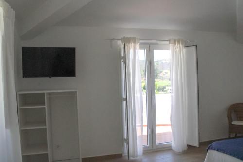 a bedroom with a tv on the wall and a window at Sudoeste Guest House in Odeceixe