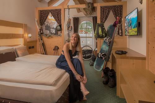 uma mulher sentada numa cama num quarto com um snowboard em Hotel Chalet Sas Morin em Pozza di Fassa