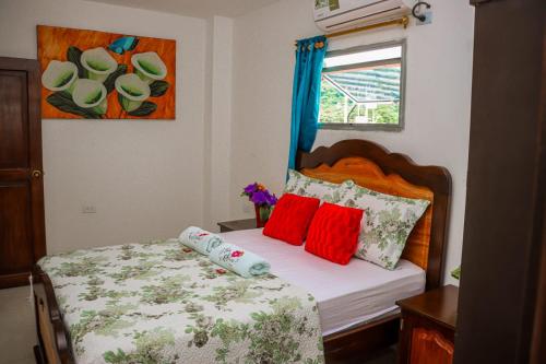 Habitación pequeña con cama con almohadas rojas en Hotel Flor Gloria en Palomino