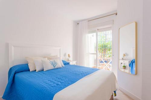 a white bedroom with a blue bed and a window at FARO PUERTO ESTEPONA in Estepona