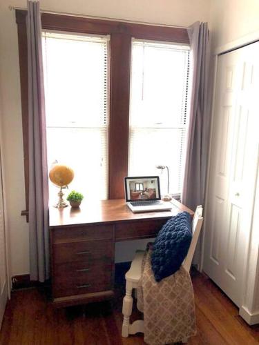 a desk with a laptop on it in a room with two windows at Beautiful 3 Bedroom Home Cozy Front and Back Porch in Munhall