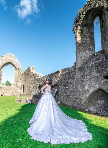 a woman in a wedding dress standing in front of a ruin at Abbey Hotel Roscommon in Roscommon