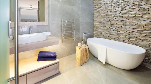 baño con bañera blanca y pared de piedra en Beachfront Penthouse Ballito, en Ballito