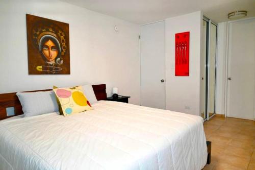 a bedroom with a white bed and a painting on the wall at Apartamento frente a la Playa Arecibo Puerto Rico in Arecibo