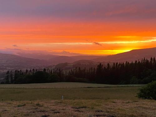 einen Sonnenuntergang über einem Feld mit Bäumen und Bergen in der Unterkunft Gwynfyd Bell Tent in Abergavenny