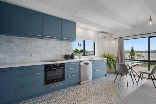 a kitchen with blue cabinets and a table and chairs at Magnificent Beachfront Mansion - Pool - Fireplace in Auckland