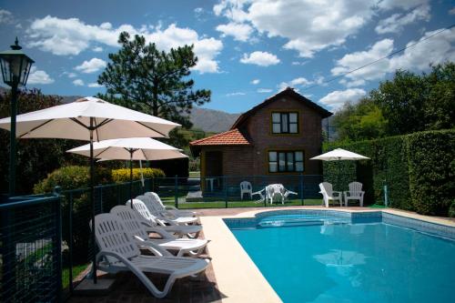 a pool with chairs and umbrellas next to a house at Cabañas Monteolivos in Merlo