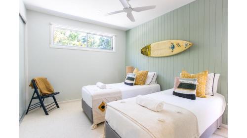 two beds in a room with a surfboard on the wall at Fennes On Banzai in Kingscliff