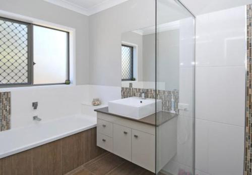 a white bathroom with a sink and a shower at Two Storey Beach House in Hervey Bay