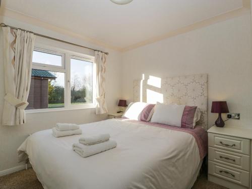a bedroom with a white bed with two towels on it at Harvester Lodge in Puxton