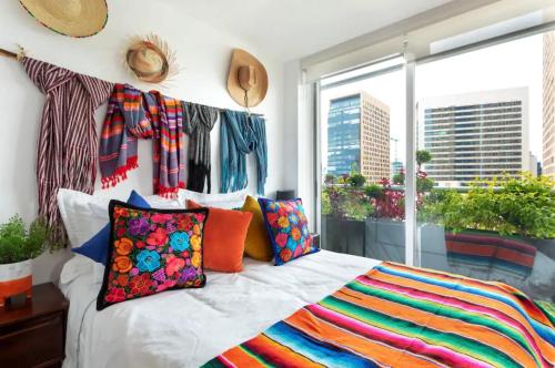a bedroom with a bed with colorful pillows and a window at Departamento mexicano en Polanco. Pool - gym - parking in Mexico City