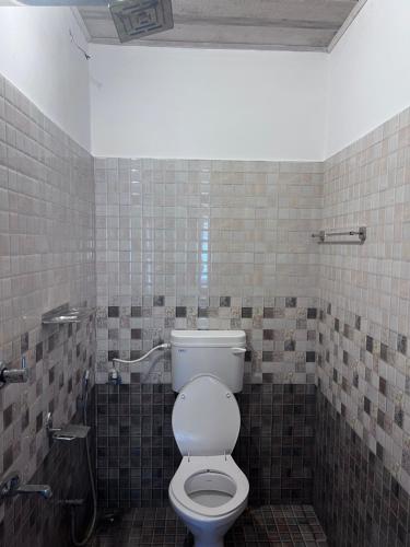 a bathroom with a toilet and a tiled wall at Hammock Beach Home in Alleppey
