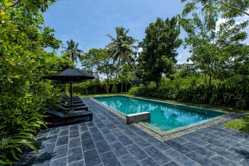 an outdoor swimming pool with an umbrella and trees at Splendour Residence in Balapitiya
