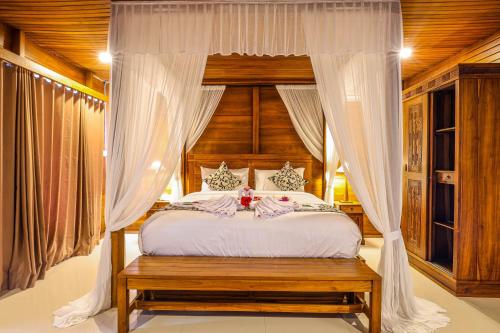BB Resort Villa and Spa في نوسا بينيدا: غرفة نوم مع سرير مظلة مع ستائر بيضاء