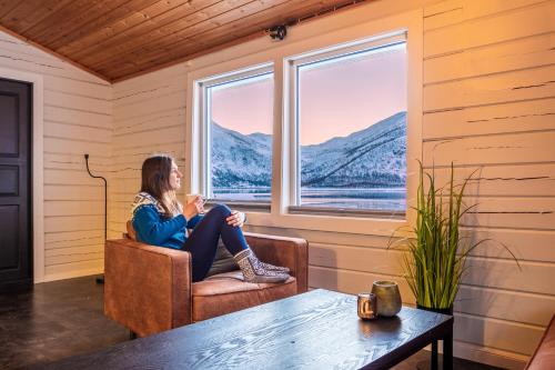 a woman sitting in a chair looking out a window at Senja Fjordcamp in Torsken