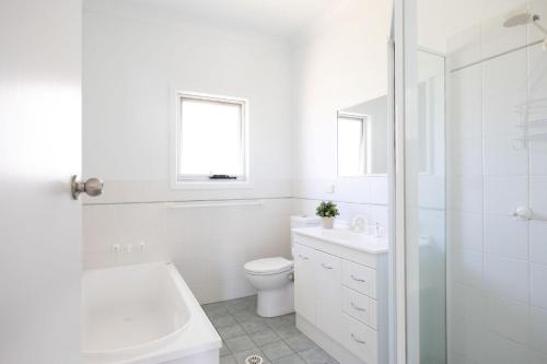 a white bathroom with a tub and a toilet and a sink at Seaside Beach House in Burrill Lake