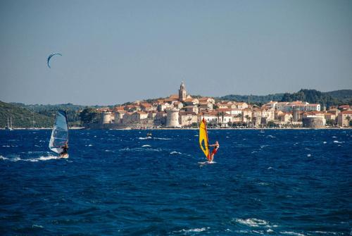 two people are windsurfing in the water with a city in the background at Lulak Studio Apartments in Orebić