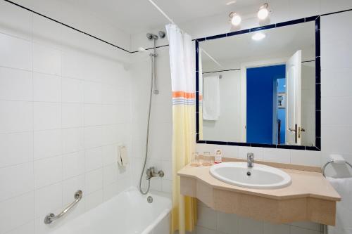 uma casa de banho com um lavatório, uma banheira e um espelho. em Sol Sancti Petri Aparthotel em Chiclana de la Frontera