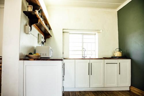 a kitchen with white cabinets and a window at Bokrivier Cottages in Greyton