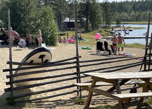 a group of people on a beach with picnic tables at Angsjöns Camping in Bjurholm