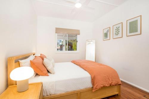 ein weißes Schlafzimmer mit einem Bett mit einer orangefarbenen Decke in der Unterkunft Fishery Road Cottage Pet Friendly 2 Mins Walk to Beach in Currarong