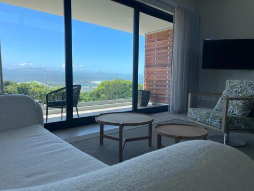 a bedroom with a bed and tables and a large window at Hilltop Bayview Luxury Apartments in Plettenberg Bay