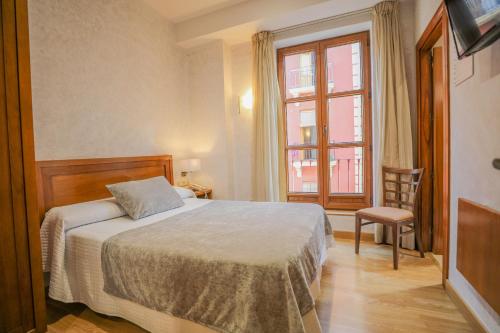 um quarto com uma cama, uma janela e uma cadeira em Hotel Granada Centro em Granada