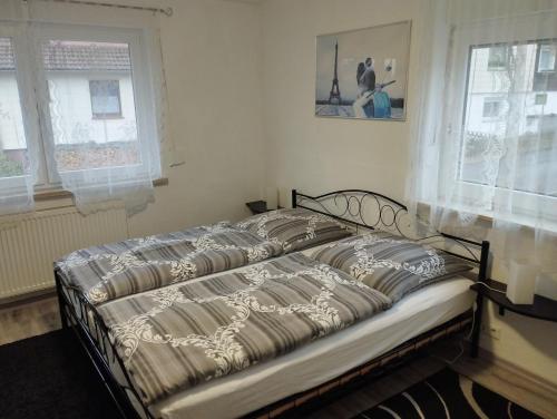 a bed sitting in a bedroom with two windows at Harzpension Haus Königskopf in Braunlage