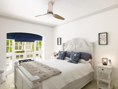 a white bedroom with a white bed with blue pillows at Sago Garden Apartment at Royal Westmoreland in Saint James