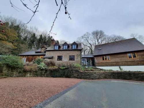 une grande maison avec un mur en pierre à côté d'une allée. dans l'établissement The Hen Den, à Hopton Cangeford