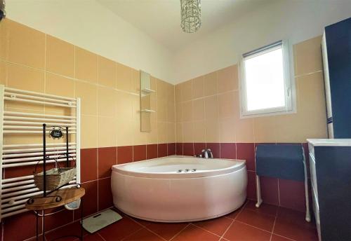 La salle de bains est pourvue d'une grande baignoire blanche et d'une fenêtre. dans l'établissement Villa au calme tout confort, à Lapalud