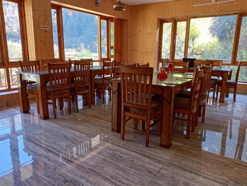 un comedor con mesas y sillas de madera y ventanas en RRR RESORTS TIRTHAN Valley by RRR HOTELS & RESORTS en Banjār