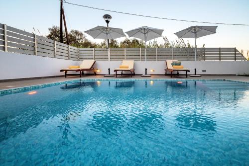 a swimming pool with chairs and umbrellas on a building at Seabreeze Villa - with Jacuzzi & heated pool in Mastichari