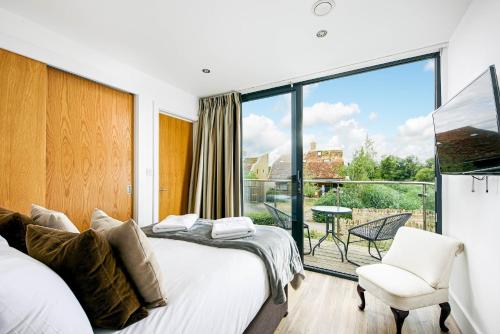 ein Schlafzimmer mit einem Bett und einem Stuhl und einem großen Fenster in der Unterkunft Lakeside roof terrace with Spa access Le Mirage in Somerford Keynes