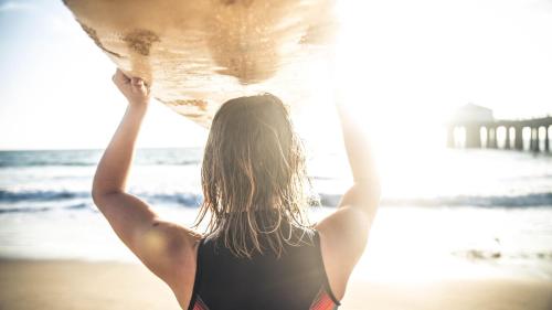 a woman standing on the beach holding a surfboard at GreenTree Inn San Diego Mission Bay in San Diego