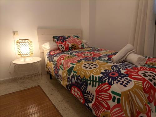 Un dormitorio con una cama con un edredón colorido y una lámpara. en Apartamento playa de Levante, en La Línea de la Concepción
