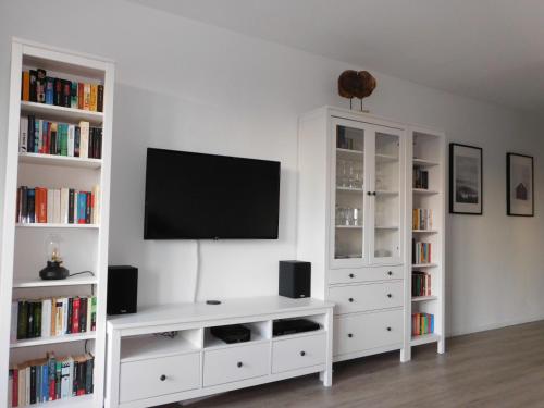 uma sala de estar branca com uma televisão e prateleiras de livros em Harzbude em Braunlage