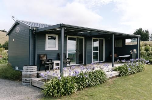 a green tiny house with a patio and flowers at Birds Eye View in Havelock North