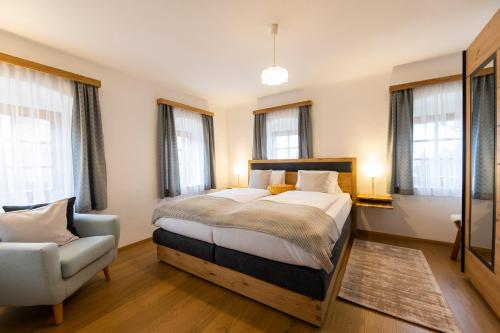 a bedroom with a bed and a chair and windows at Das Ferienhaus mit Sauna! Neu renoviertes "Liebler Heimathaus" mit Sauna aus Zirben-Altholz, einer "Styrian Whisky Relaxing Lounge" sowie großer Panoramaterrasse! 