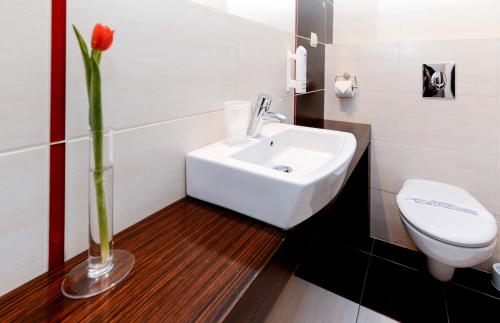 łazienka z białą umywalką i wazą z czerwonym kwiatem w obiekcie Hotel Liburnia w mieście Cieszyn