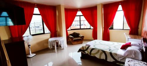 1 dormitorio con cortinas rojas, 1 cama y 1 silla en Hostal Carolina, en Yantzaza