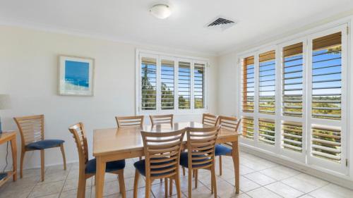 Un comedor con mesa y sillas y ventanas. en Myall River Views - 66 The Anchorage, en Hawks Nest